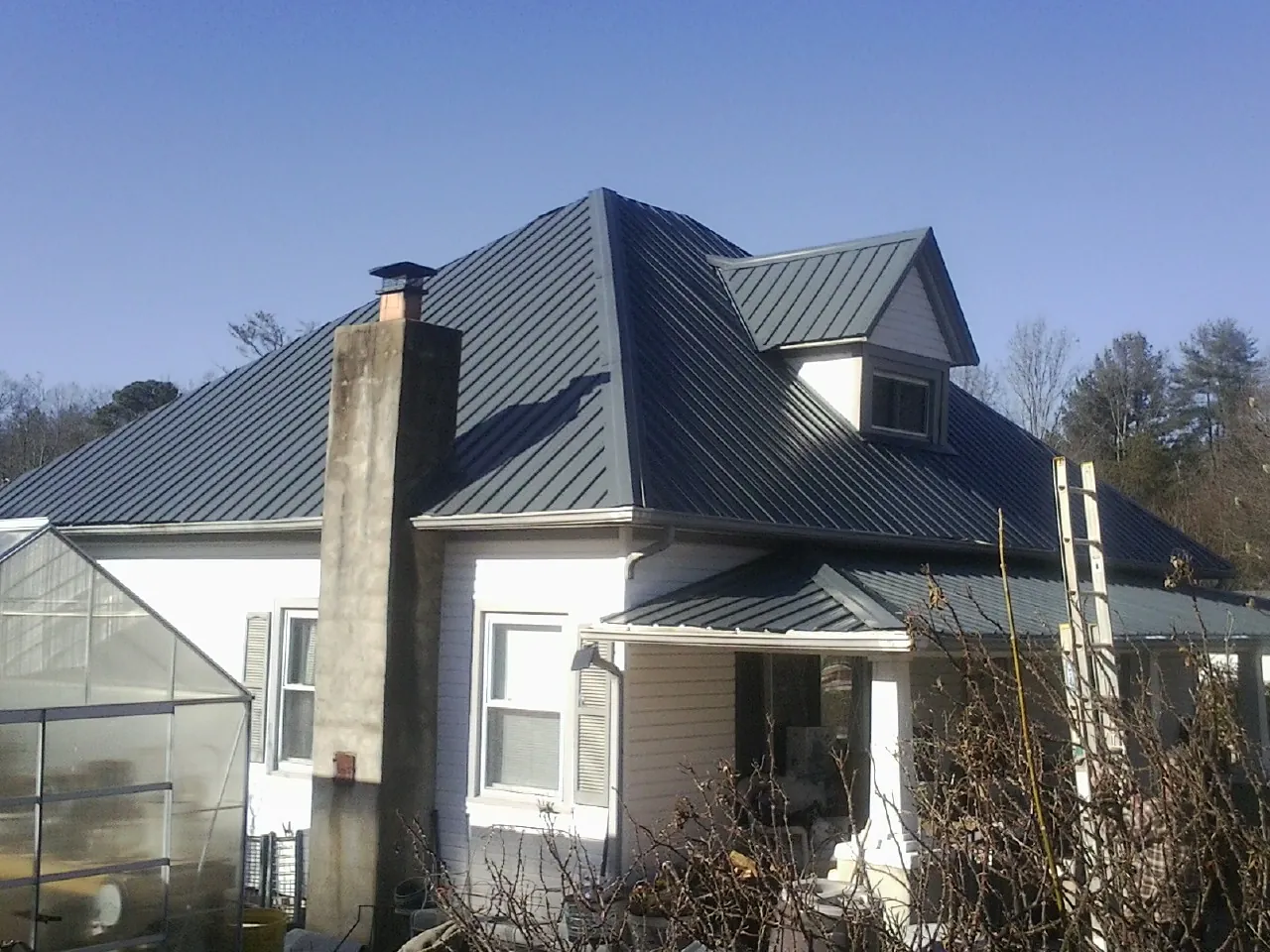Dark blue standing seam metal roof on a white farmhouse with dormer — Slate & Tile Roof Repair by Roofing Brothers in Maceo