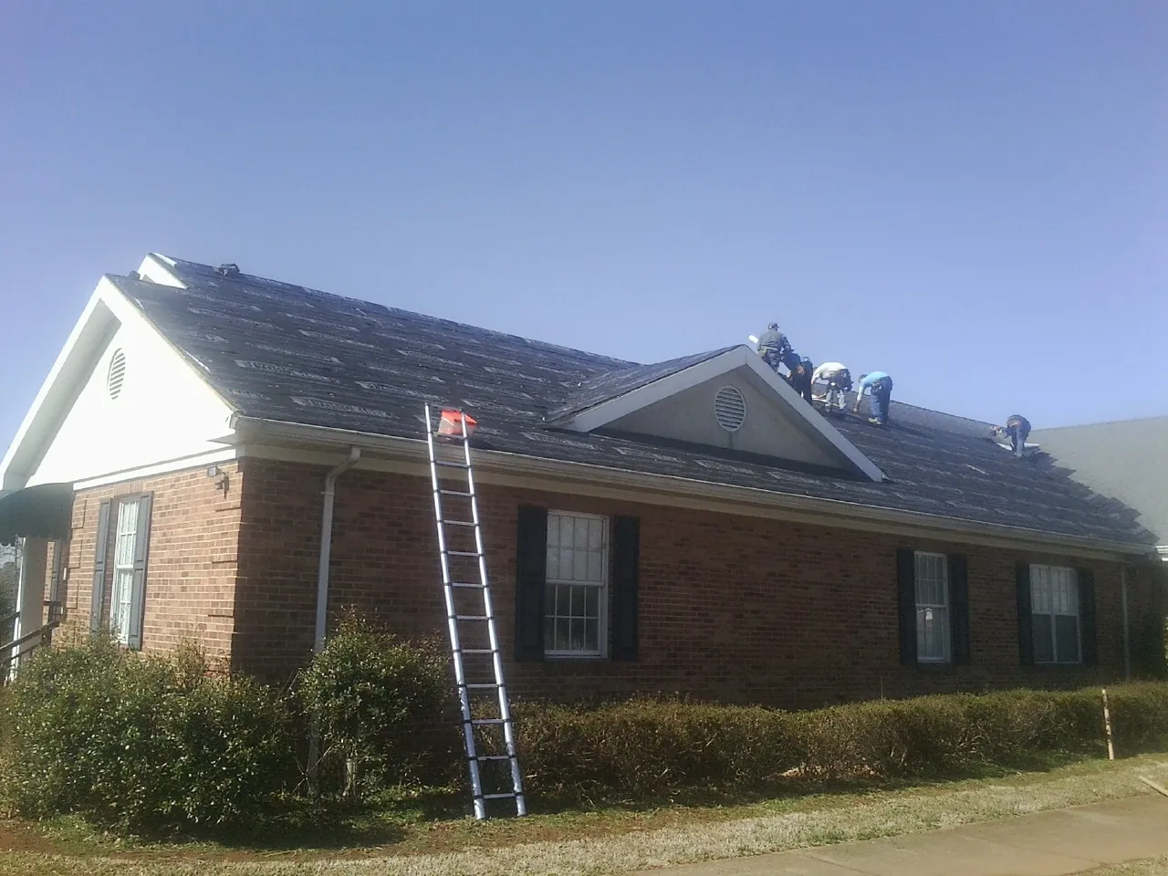 Crew tearing shingles off a brick ranch roof with a ladder set — Metal Roof Repair work by our crew in Maceo