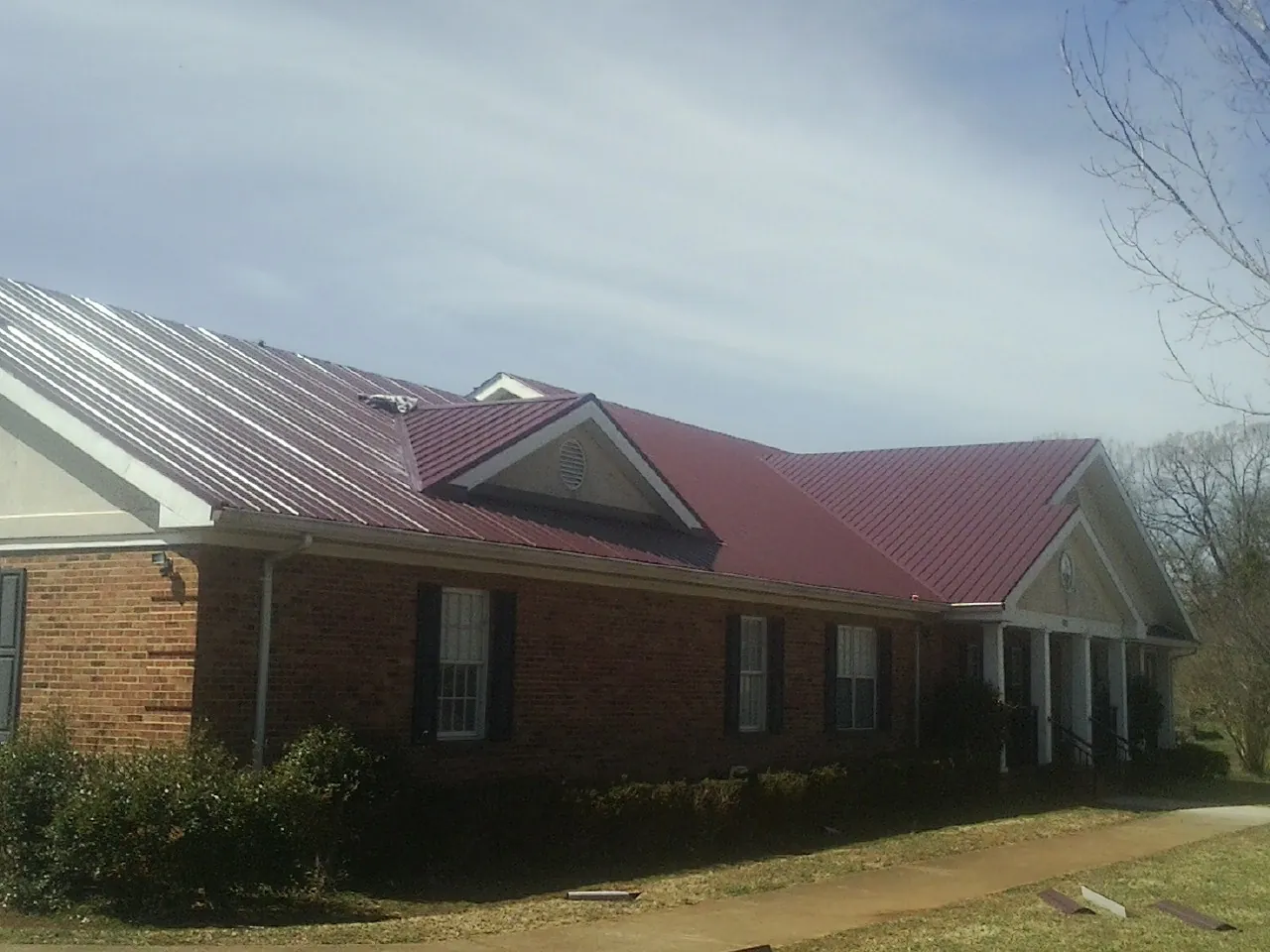 Red metal roof with gabled entries on a long brick building, from a Hail Damage Roof Repair job in Maceo