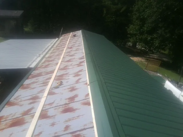Old rusted panels beside newly installed green metal roofing — Wind Damage Roof Repair by Roofing Brothers in Maceo