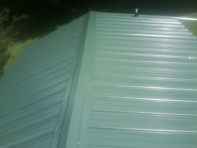 New green metal panels meeting at the ridge of a roof — Flat Roof Repair work by our crew in Maceo