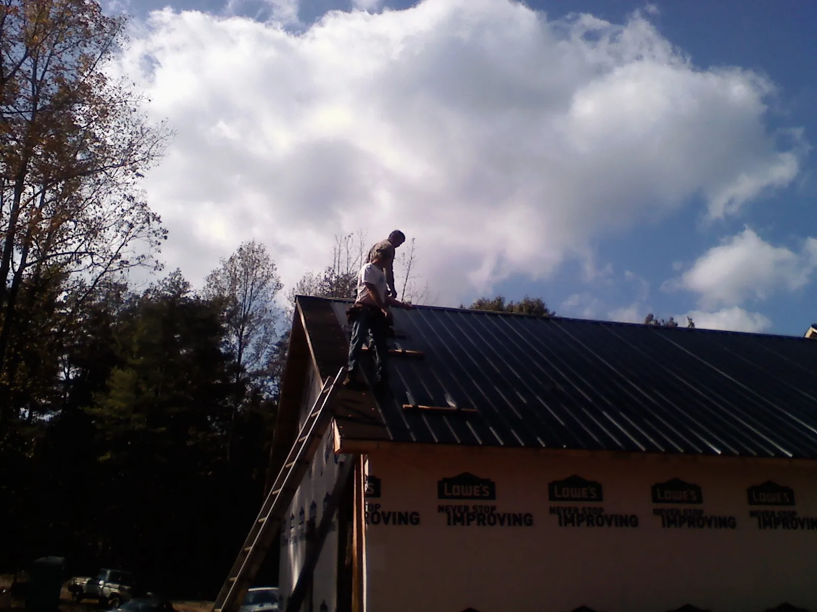 Roofer fastening dark metal panels high against a cloudy sky, from a Roof Inspection job in Maceo