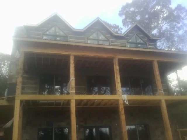 Dormers and porch framing on a large log home under construction — Roof Coating work by our crew in Maceo