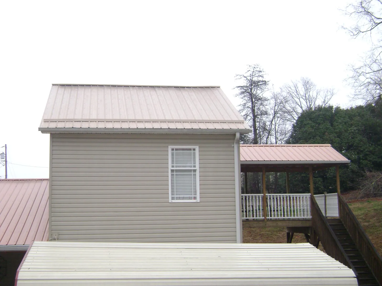 Tan metal roofs on a two story addition and attached porch, from a Roof Replacement job in Maceo